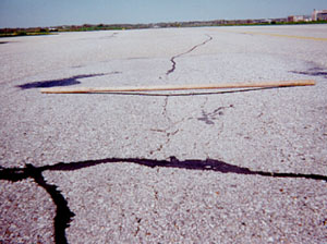 Overview photo of a pavement with a visible area of high-severity rutting.            A 6-ft (2-m) long piece of wood has been placed across the rut to show the depth of the rut.