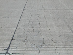 Overview photo of a PCC slab with a noticable pattern of fine cracks spread over the entire surface area of the slab.            Some of the cracks are spalled.