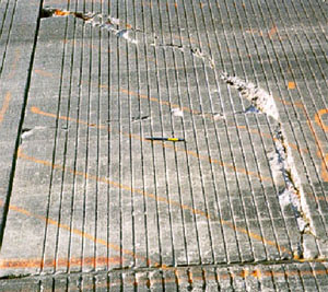 Close-up photo of a PCC slab corner with a high-severity corner break. The corner break is broken into two pieces, has considerable spalling, and has noticable faulting.