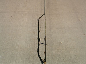 Close-up photo of a low-severity joint spall.  The spall is a farily long but narrow spall, and is defined by a single medium-severity crack.
