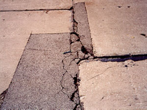 Close-up photo of an irregularly shaped asphalt patch within a PCC slab.  The patch           contains considerable visible distress that includes spalling, cracking, and a noticable loss of material.